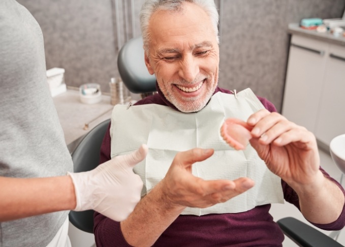 Smiling senior man in dental chair holding a denture
