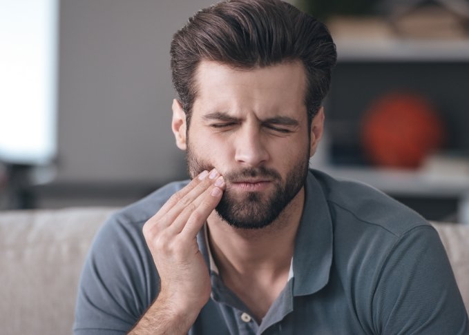 Man holding his cheek and wincing in pain