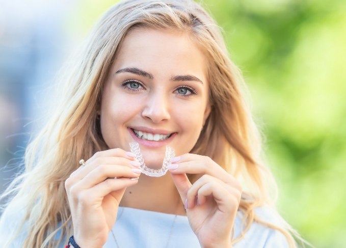 Smiling blonde woman holding an Invisalign tray