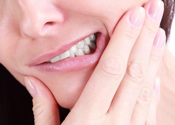 Close up of person holding their cheek in pain before tooth extraction