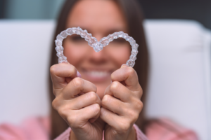 Woman holding up two Invisalign trays to form a heart