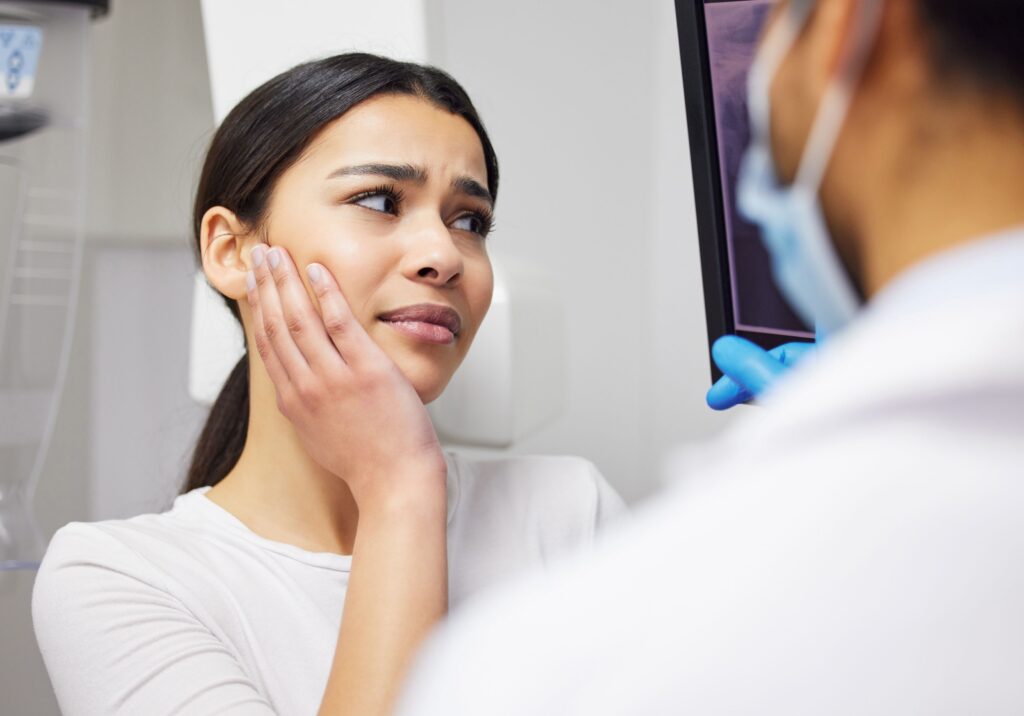 Woman holding her hand to her face as dentist goes over her x-rays