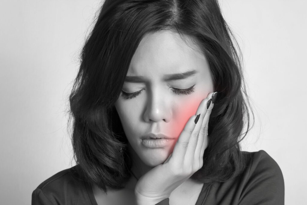 Grayscale image of woman pressing hand to sore cheek highlighted red