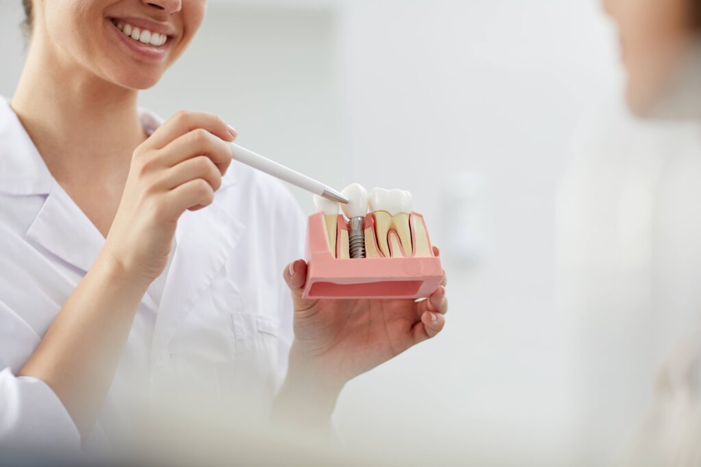 Smiling dentist pointing to model of dental implant